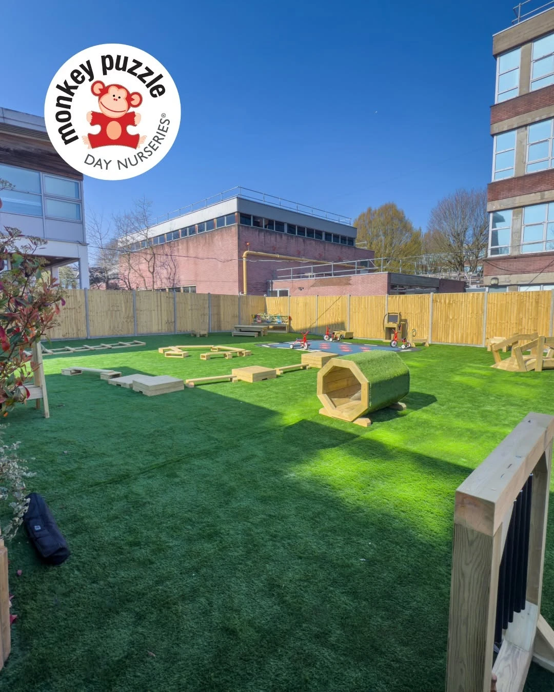 Outdoor nursery play area with artificial grass, timber equipment and fencing
