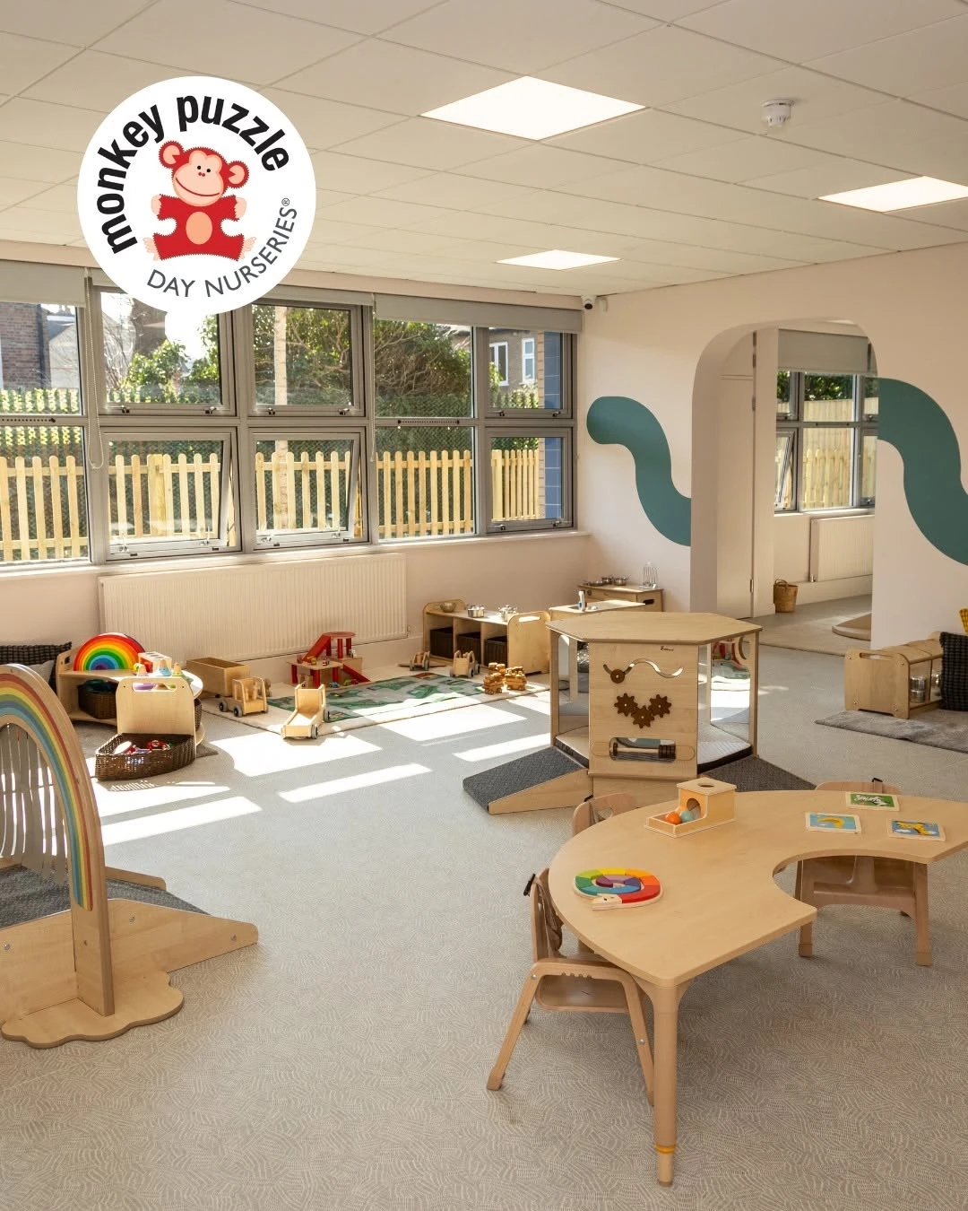Sunlit nursery room with low shelves, activity tables and teal wall details