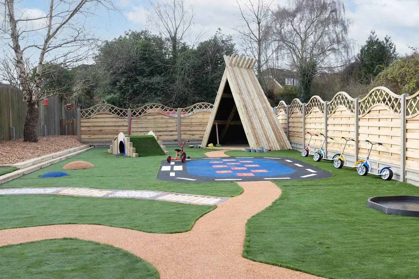 Nursery garden with a timber play shelter, activity markings and planted boundaries