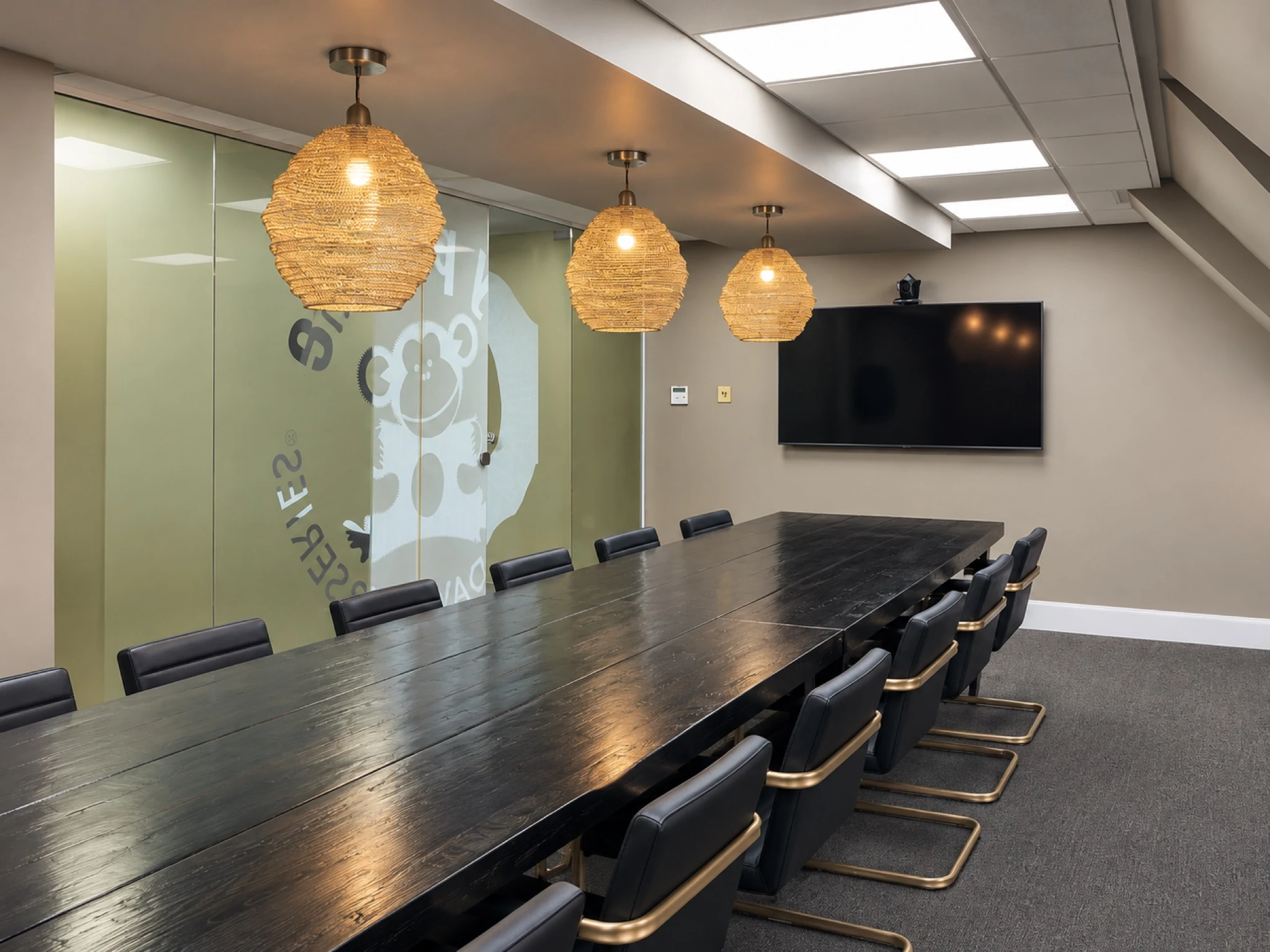 Boardroom with a long meeting table, woven pendant lights and glazed partitions.