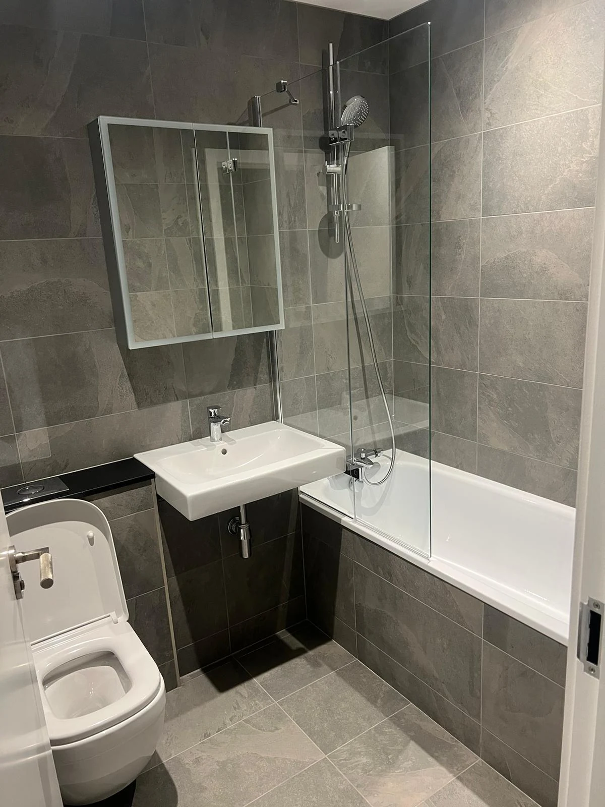 The finished bathroom with tiled walls and a glazed bath screen.