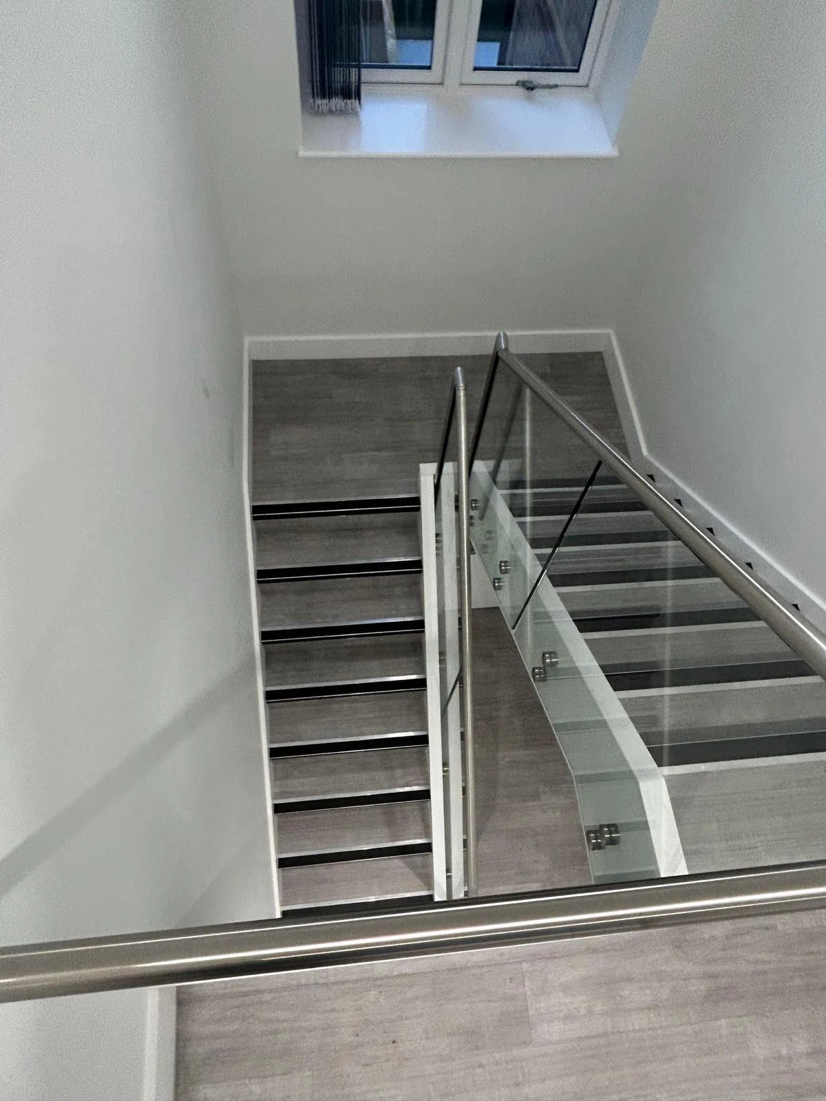 The completed staircase with glass balustrades and metal handrails.