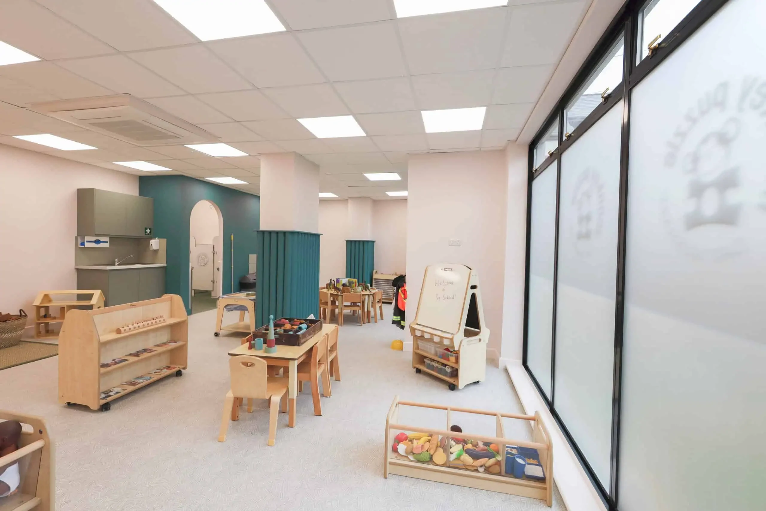 Nursery learning room with glazed partitions, low timber furniture and teal wall details