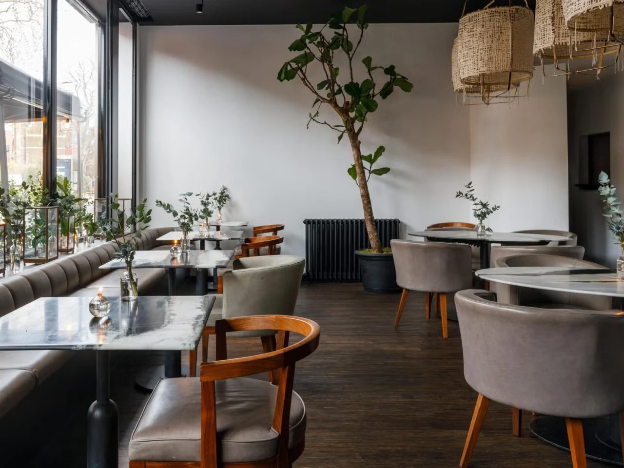 Window-side banquette seating, marble tables and indoor greenery at Angelina Dalston